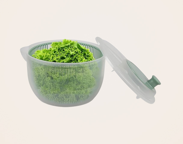 Ein transparenter Behälter mit frischem, grünen Kopfsalat, der teilweise mit einem Deckel abgedeckt ist. Der Behälter hat innen ein Gittermuster, das die Salatblätter hält.