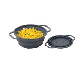 Graues, zusammenklappbares Silikon-Abtropfsieb mit Griffen, aufgeklappt und mit gelben Penne-Nudeln gefüllt; daneben ein eingeklapptes Sieb.