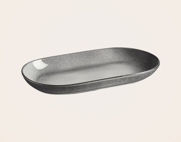 Eine ovale, flache Schale in mattem Schwarz mit einer glänzenden, weißen Stelle an einem Rand. Die Schale hat sanfte, abgerundete Kanten und eine schlichte, elegante Form. Sie eignet sich für das Servieren von Speisen oder als dekoratives Element.