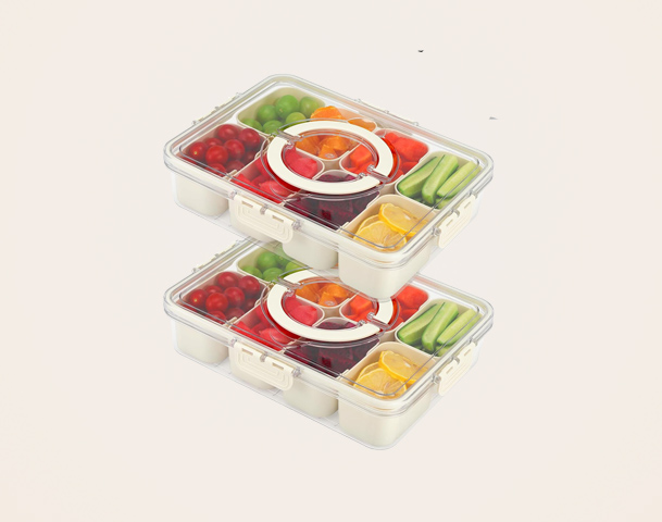 Zwei stapelbare Lunchboxen aus durchsichtigem Kunststoff, gefüllt mit einer Vielzahl von frischem Obst und Gemüse. Dazu gehören Kirschtomaten, Trauben, Paprika, Gurken und Zitrusfrüchte. Die Boxen sind in verschiedenen Fächern unterteilt, um die Lebensmittel zu trennen.
