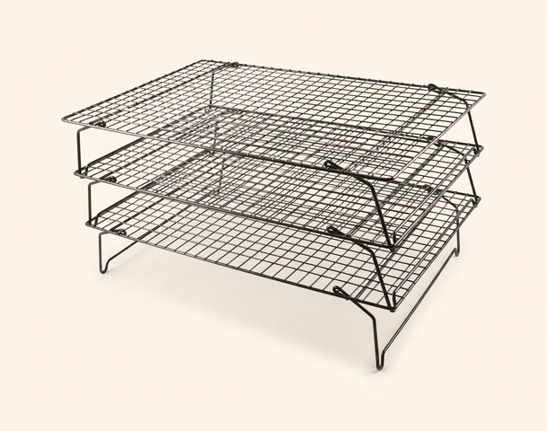 Ein dreistufiges Gitterregal aus Metall. Die Regale sind aus feinen, kreuzförmigen Drähten gefertigt und bieten eine stabile Unterlage. Es ist in der Mitte offen, um eine gute Luftzirkulation zu ermöglichen, und auf abgewinkelten Beinen montiert, die dem Regal Halt geben.