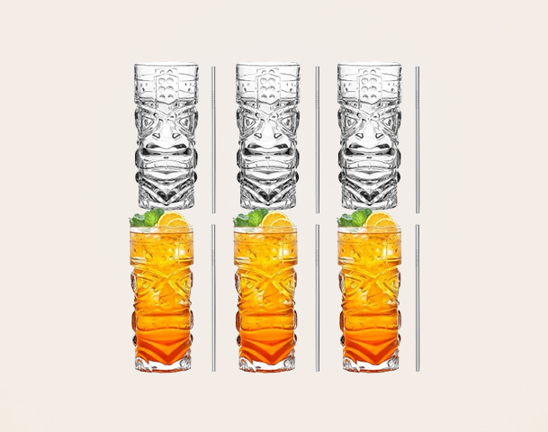 Sechs farbige Trinkgläser mit Tiki-Muster sind abgebildet. Oben stehen zwei leere Gläser, darunter vier gefüllte Gläser mit einem orangefarbenen Getränk, verziert mit einem Minzblatt und einer Zitronenscheibe. Die Gläser sind auf einem hellen Hintergrund angeordnet.