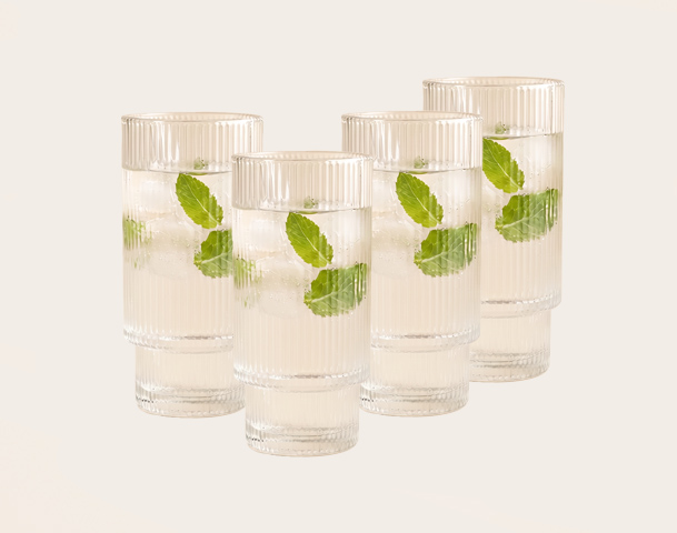 Ein zeitgenössisches Glas mit einem kühlen Getränk, gefüllt mit Eiswürfeln und frischen Minzblättern. Die Glasoberfläche hat eine gerippte Struktur, die dem Design eine elegante Note verleiht. Der Hintergrund ist neutral und hebt das Glas hervor.