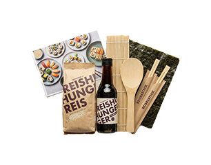 Sushi-Set: Packung Reishunger-Reis, Flasche Reisessig, Bambus-Sushimatte, Reislöffel und -schaufel, Holzstäbchen, Nori-Algenblätter und Anleitung mit Sushi-Fotos.