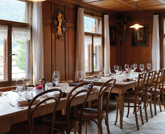 Ein einladender Restaurantbereich mit Holztischen und Stühlen. Die Tische sind für Gäste gedeckt, mit Gläsern und Besteck. Durch die Fenster fällt Tageslicht, während dekorative Elemente an den Wänden eine gemütliche Atmosphäre schaffen.