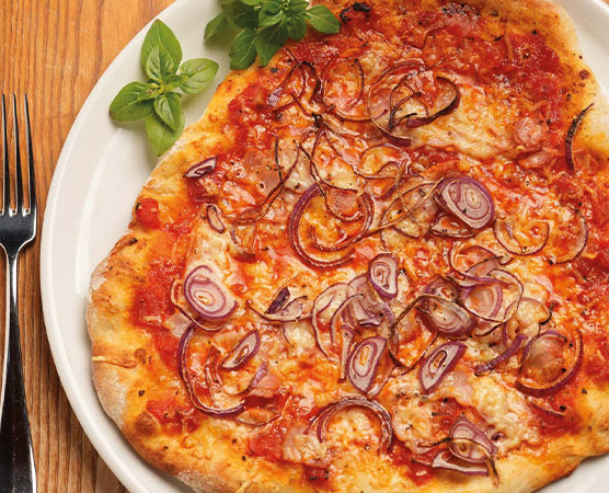 Eine frisch gebackene Pizza auf einem weißen Teller, belegt mit Tomatensauce, geschmolzenem Käse und rohen Zwiebelringen. Einige grüne Basilikumblätter sind danebengelegt. Der Pizzarand ist knusprig und goldbraun.