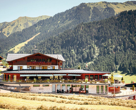Ein modernes Chalet im Alpenstil, umgeben von beeindruckenden Bergen und dichten Wäldern. Die Terrassen des Gebäudes laden zum Entspannen ein, während die sonnige Landschaft eine idyllische Bergatmosphäre schafft.