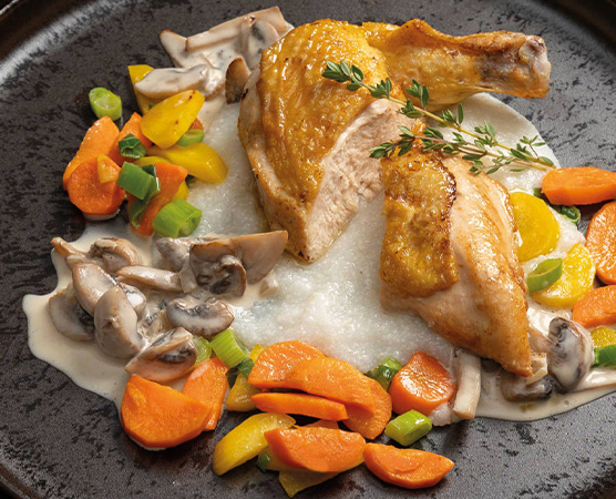 Ein Teller mit gebratenem Hähnchenschenkel, garniert mit frischen Thymianzweigen. Daneben sind pürierte Kartoffeln und eine bunte Beilage aus Karotten, gelben Paprika, Frühlingszwiebeln und Champignons zu sehen. Die Anordnung der Speisen ist ansprechend und verleiht dem Gericht ein einladendes Aussehen.