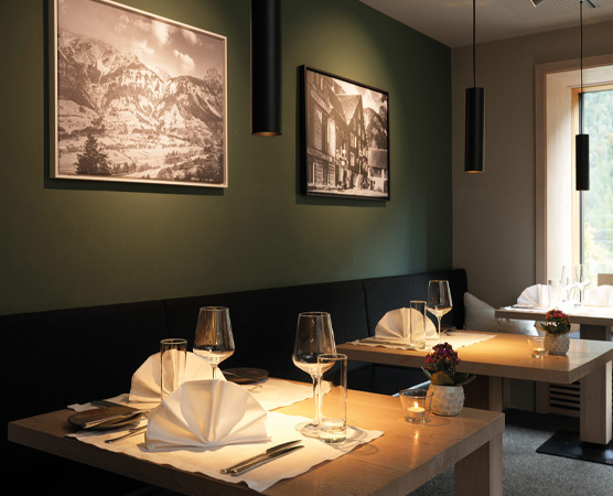 Das Bild zeigt ein elegantes Restaurant mit zwei Tischen, die festlich eingedeckt sind. Jeder Tisch hat Gläser, Besteck und kunstvoll gefaltete Servietten. An den Wänden hängen Schwarz-Weiß-Fotografien von Landschaften und historischen Gebäuden. Die Atmosphäre wirkt gemütlich und einladend.