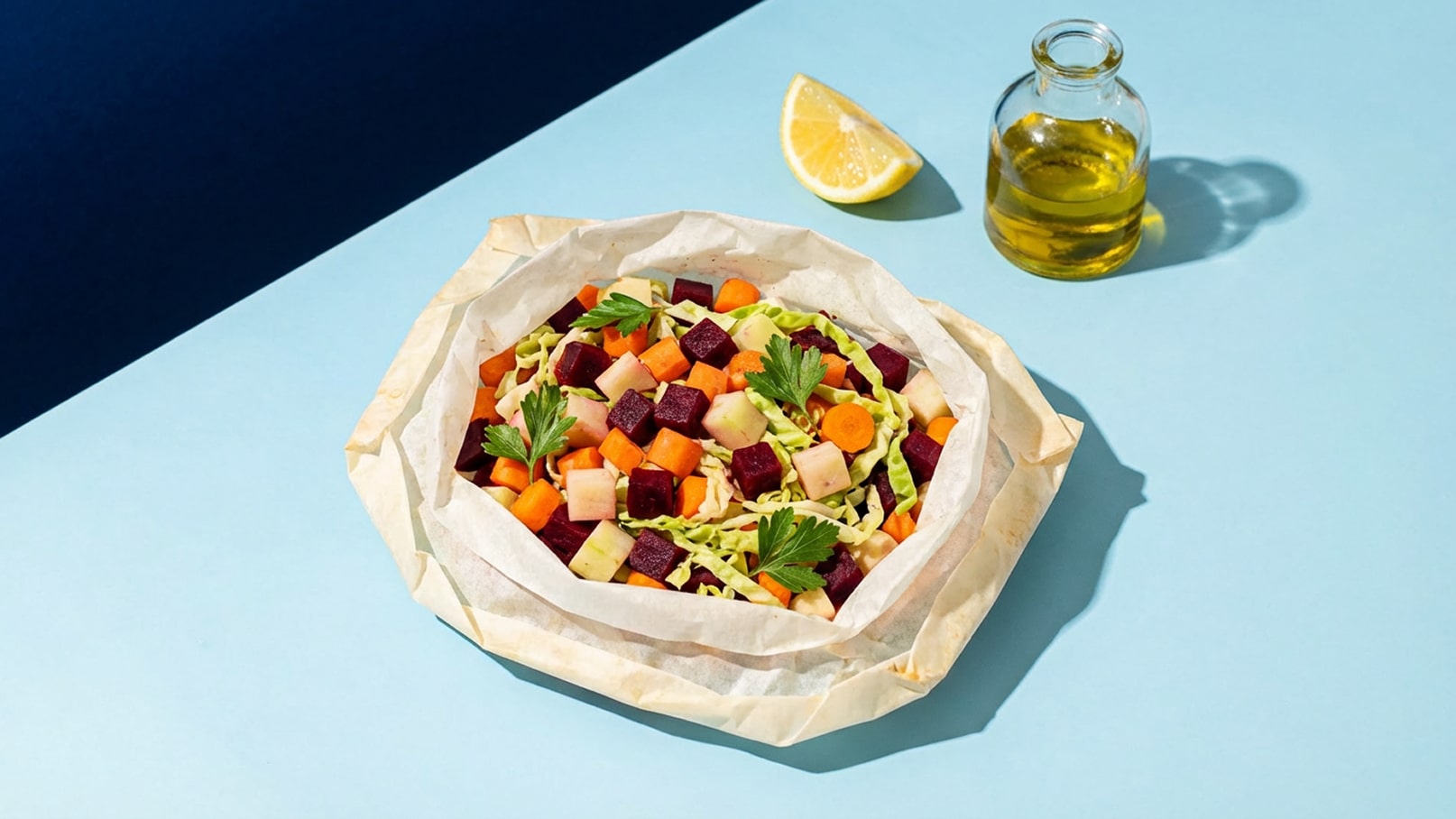 Eine Schüssel mit buntem Gemüsesalat, bestehend aus Roter Beete, Karotten, Apfelstücken und grünen Blättern, die in Backpapier serviert wird. Neben der Schüssel liegt eine Limettenscheibe und eine Flasche Olivenöl.