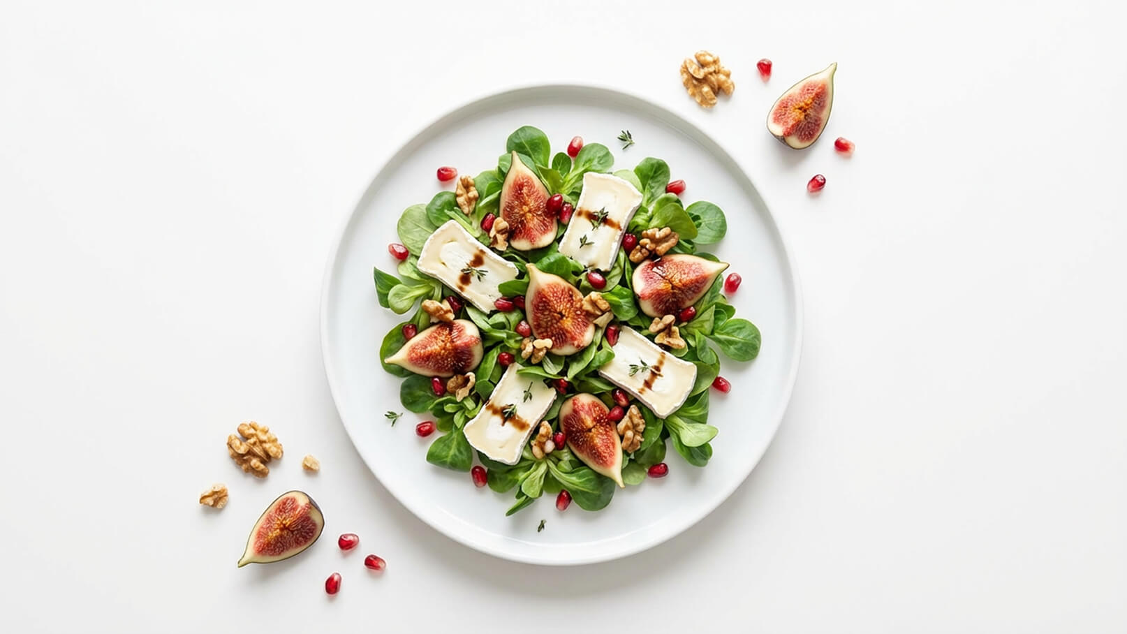 Eine Schüssel Salat mit frischem Blattgemüse, belegt mit Feigen, Walnüssen, Granatapfelkernen und Stückchen von Ziegenkäse. Die Zutaten sind ansprechend angeordnet und mit einer Balsamico-Reduktion verfeinert.