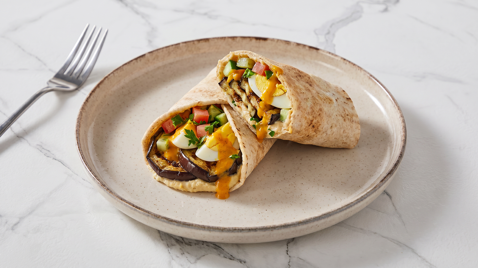 Auf einem beigefarbenen Teller liegt ein aufgerollter Wrap. Er ist mit gegrilltem Gemüse, Käse, Eiern und frischen Tomaten gefüllt. Daneben liegt eine Gabel. Der Hintergrund ist marmoriert und hell.