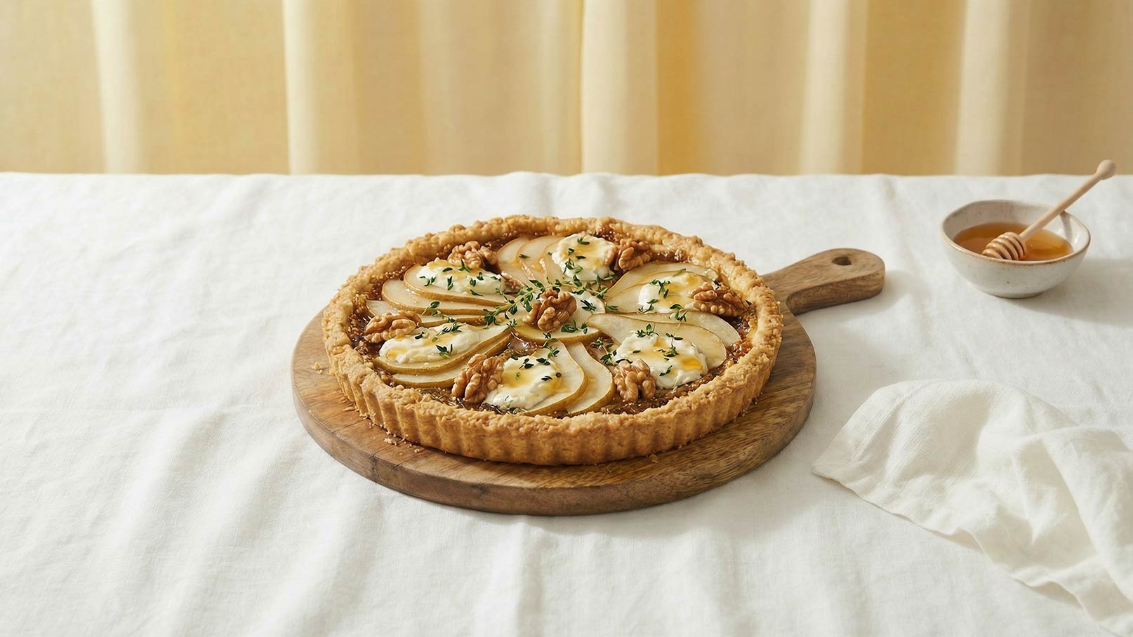 Eine Tart auf einem Holzbrett, belegt mit dünnen Apfelscheiben und Nüssen, ist dekoriert mit einer cremigen Schicht und frischen Kräutern. Im Hintergrund befindet sich eine kleine Schüssel mit Honig. Die Szenerie ist hell und freundlich, mit einem sanften, neutralen Hintergrund.