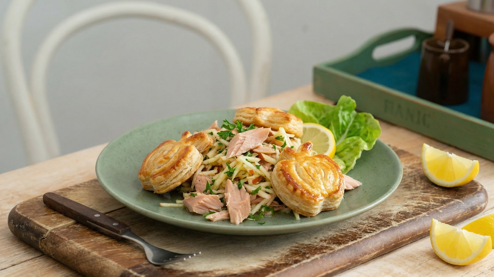 Ein Teller mit einer Portion Salat aus geriebenem Gemüse und Thunfisch. Darauf befinden sich mehrere goldbraun gebackene Teigstücke. Neben dem Teller liegen Zitronenscheiben und ein Blatt Salat. Der Hintergrund ist hell und neutral.