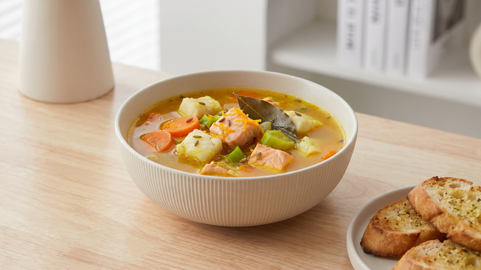 Eine Schüssel mit buntem Gemüsesuppe, die Kartoffeln, Karotten und Lauch enthält. Daneben liegt ein Teller mit knusprigem, geröstetem Brot. Die Szene vermittelt eine gemütliche Essensatmosphäre.