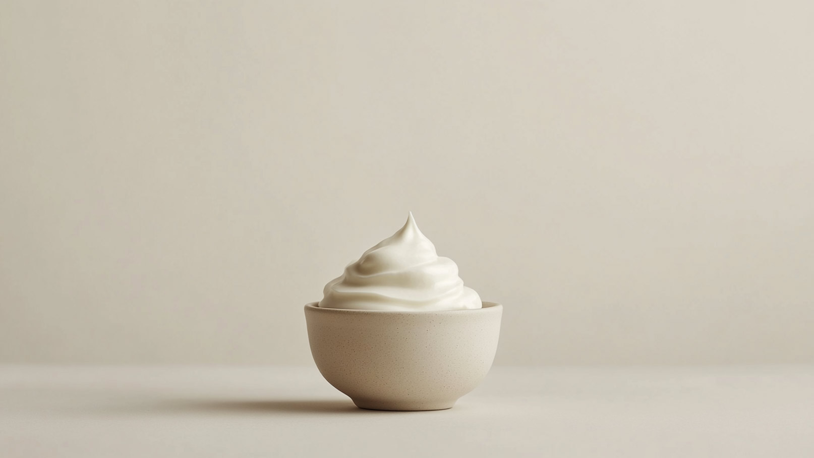 Eine helle Schüssel enthält eine große Portion schaumiger, weißer Creme. Der Hintergrund ist ebenfalls neutral gehalten, wodurch die Creme besonders hervorsticht.