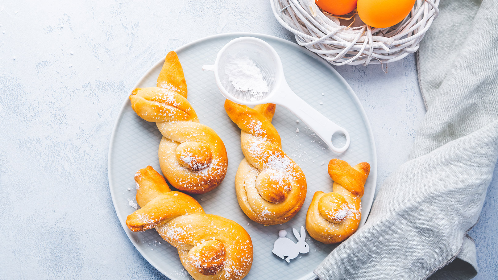 Das Bild zeigt einen eindrucksvollen Osterlammkuchen als zentrales Element, umgeben von drei kleinen Osterlämmern. Die kleinen Lämmer sind niedlich und detailreich gestaltet, und blicken fast lebendig aus. Um sie herum sind frische Himbeeren, leuchtend rote Johannisbeeren und exotische Physalis liebevoll drapiert, die dem Bild eine fruchtige Note verleihen.