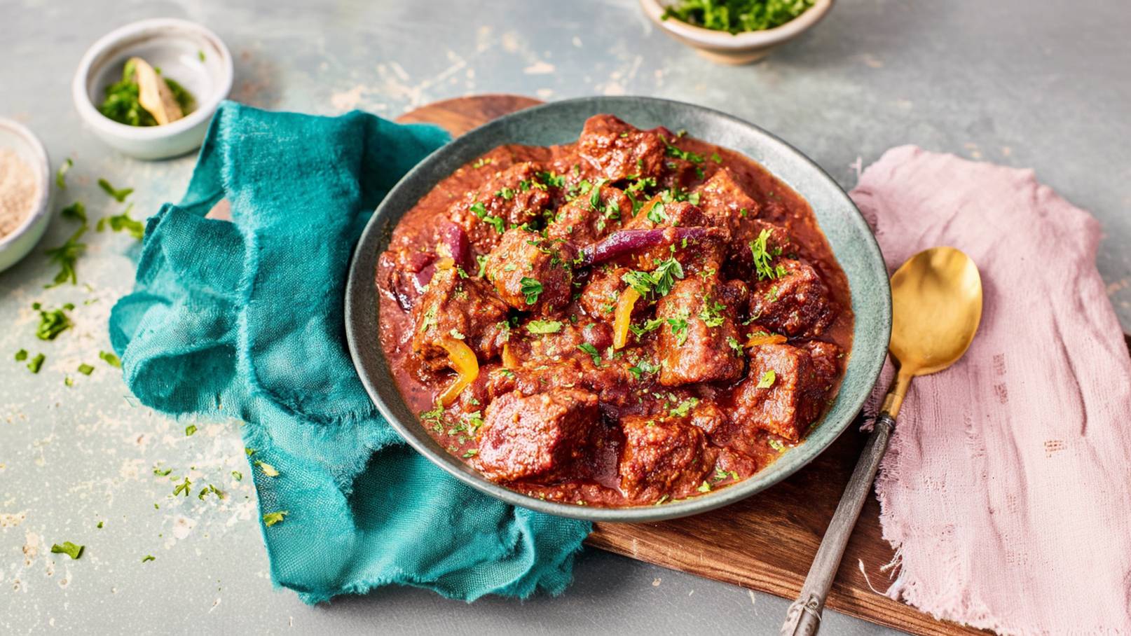 Auf dem Bild ist eine schwarze Pfanne zu sehen, gefüllt mit köstlich duftendem selbstgemachtem ungarischen Gulasch. Das Gericht ist reichhaltig, mit zarten Fleischstücken, Paprikaschoten und Zwiebeln in einer würzigen Sauce. Das Gulasch ist großzügig mit frischem Rosmarin bestreut, der dem Gericht eine aromatische Note verleiht. Neben der Pfanne liegen weitere Rosmarinzweige.
