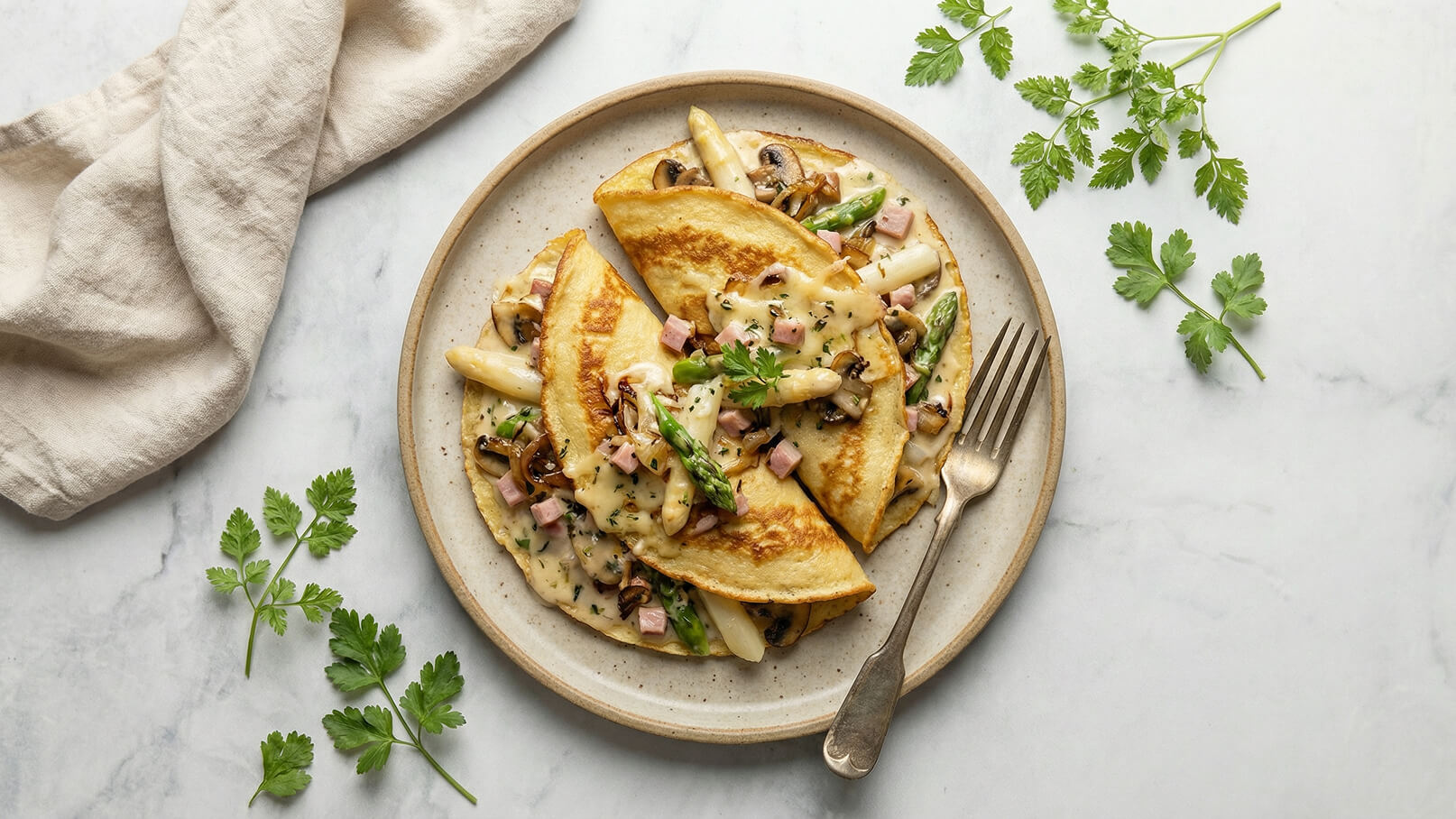 Ein Teller mit gefüllten Omelettes, die mit Spargel, Pilzen und Schinken gefüllt sind. Über den Omelettes liegt eine cremige Sauce und frischer Koriander ist als Garnitur verwendet. Die Oberfläche ist hell und einladend, serviert auf einem einfachen, runden Teller.