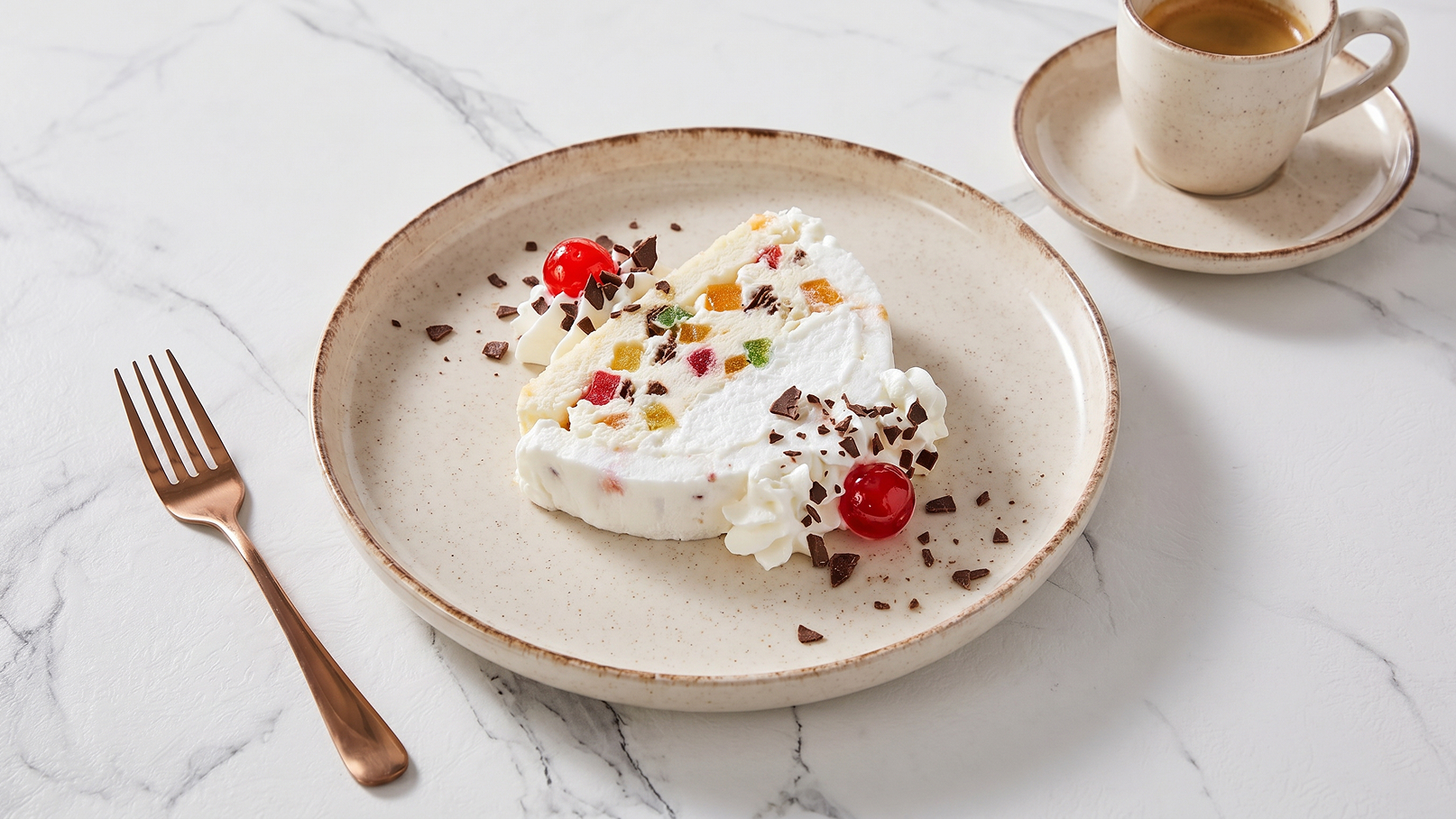 Auf dem Teller liegt ein Stück Sahnetorte, garniert mit bunten Fruchtstücken, Schokoladenstückchen und Kirschen. Daneben steht eine kleine Tasse Kaffee auf saucer. Der Hintergrund ist ein helles, marmoriertes Design.