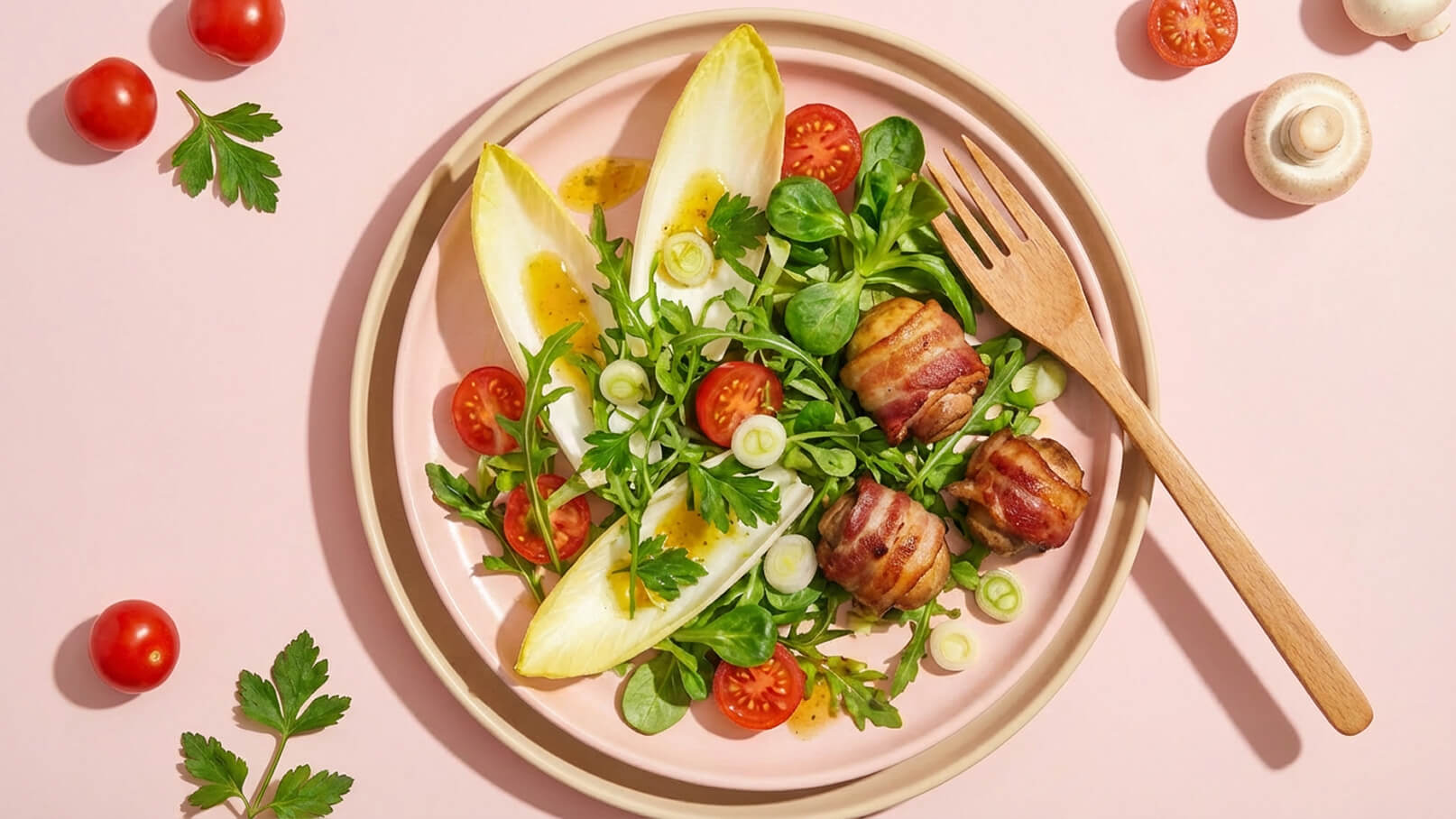 Ein Teller mit frischem Salat, garniert mit Lattich, Kirschtomaten und Kräutern. Auf dem Salat liegen umwickelte Fleischstücke. Eine Holzgabel steht neben dem Teller, der auf einem rosa Hintergrund platziert ist.