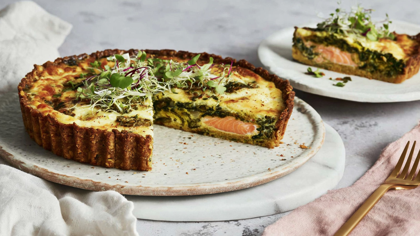 Das Bild zeigt ein rustikales Holzbrett, auf dem eine köstliche Spinat-Quiche präsentiert wird. Die Quiche ist goldbraun gebacken und zeigt eine Vielzahl frischer Spinatblätter, die appetitlich hervorsticht. Im Hintergrund ist ein grün-weiß kariertes Tuch zu sehen, das dem Bild eine frische und einladende Note verleiht.