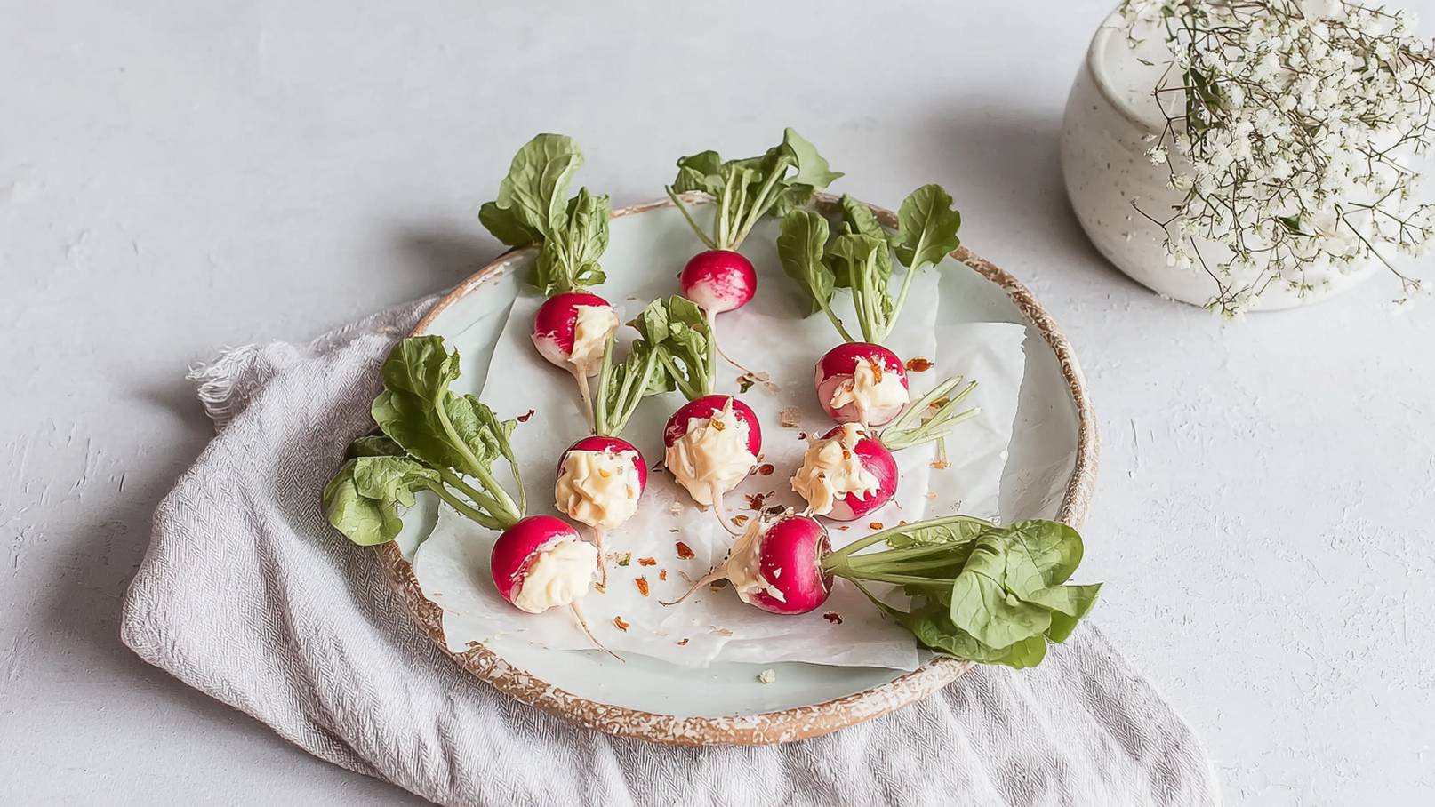 Ein runder Holz-Plateau mit acht gefüllten Radieschen, die eine cremige Füllung enthalten. Neben den Radieschen sind frische Blattgemüse zu sehen. Die Anordnung vermittelt einen frischen und einladenden Eindruck.