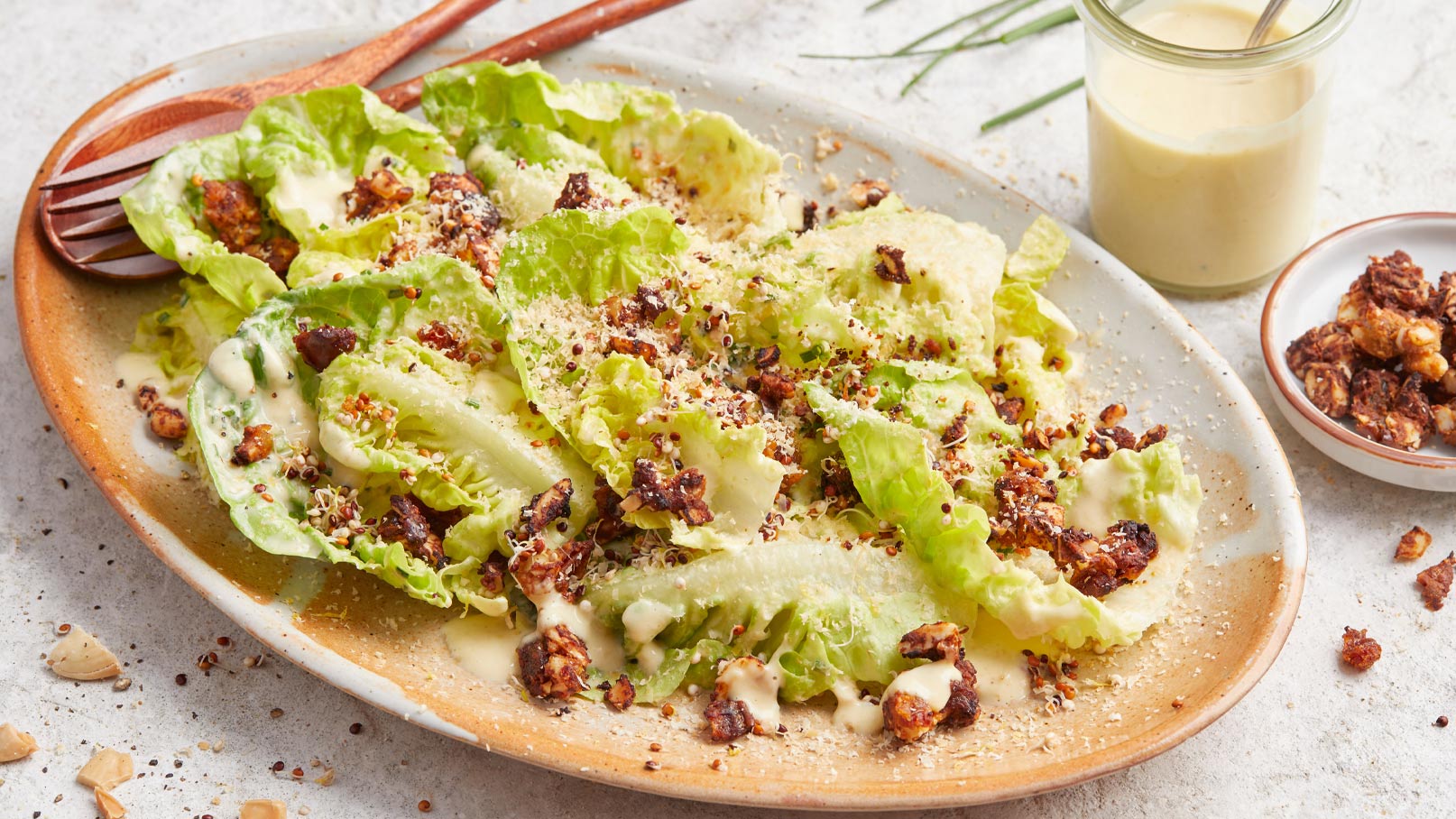 Ein Teller mit knackigem Salat, garniert mit cremigem Dressing, gerösteten Nüssen und einer Prise Käse. Der Salat besteht aus frischen, grünen Blättern und hat eine appetitliche Textur, die harmonisch mit den verschiedenen Zutaten kombiniert ist.