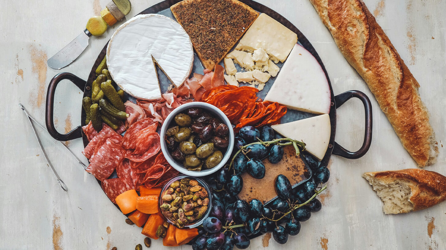 Auf einer Servierplatte angeordnet sind verschiedene Käsesorten, Wurst, Oliven, Trauben, Karotten und Nüsse. Die Platte bietet eine bunte Auswahl an Snacks, die für eine gesellige Runde geeignet sind.
