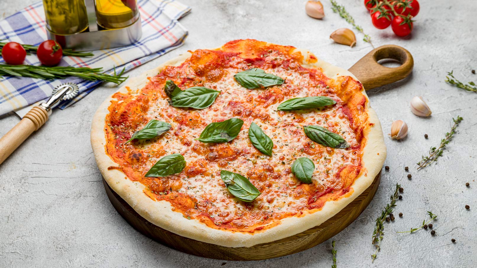 Eine frisch gebackene Pizza auf einem Holzbrett, belegt mit Tomatensoße, geschmolzenem Käse und frischen Basilikumblättern. Der Rand ist goldbraun und knusprig. Im Hintergrund sind einige Kräuter und Knoblauchzehen sichtbar.