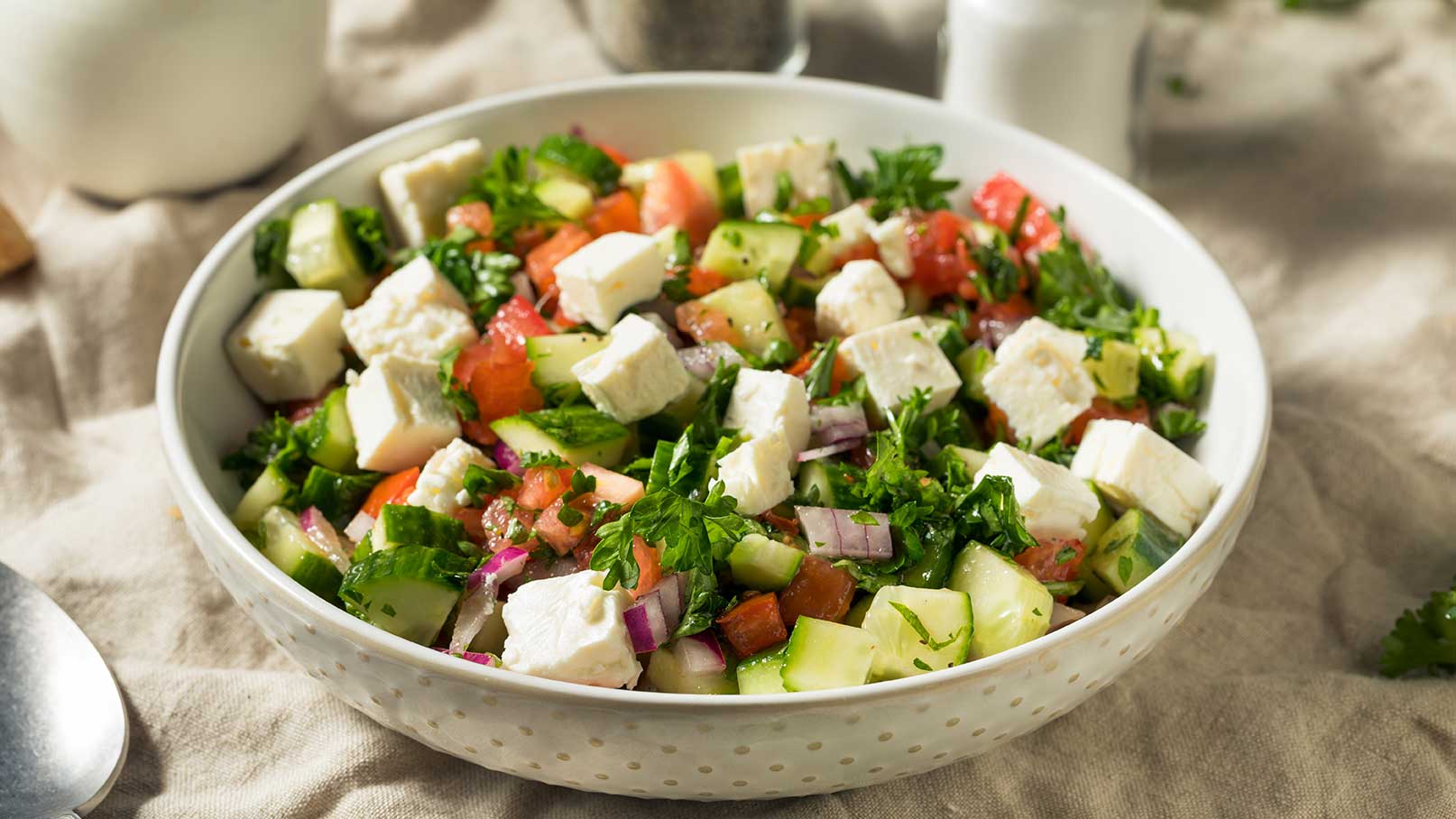 Eine Schüssel Salat mit gewürfeltem Gurke, Tomaten, roten Zwiebeln und Feta-Käse. Der Salat ist mit frischem Koriander garniert und sorgt für eine bunte, gesunde Mahlzeit.