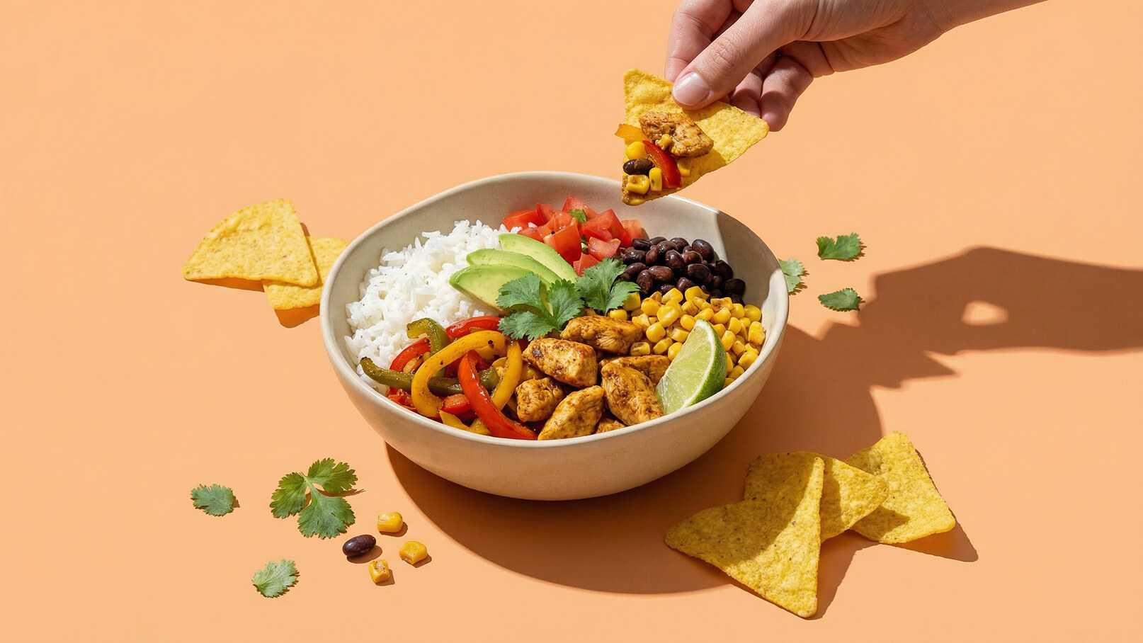 Eine Schüssel mit Reis, Hühnchen, schwarzen Bohnen, Mais, Tomaten, Avocado und buntem Gemüse. Neben der Schüssel liegt eine Hand mit einer Tortilla-Chips, bereit, das Essen aufzulockern. Der Hintergrund ist orangefarben.