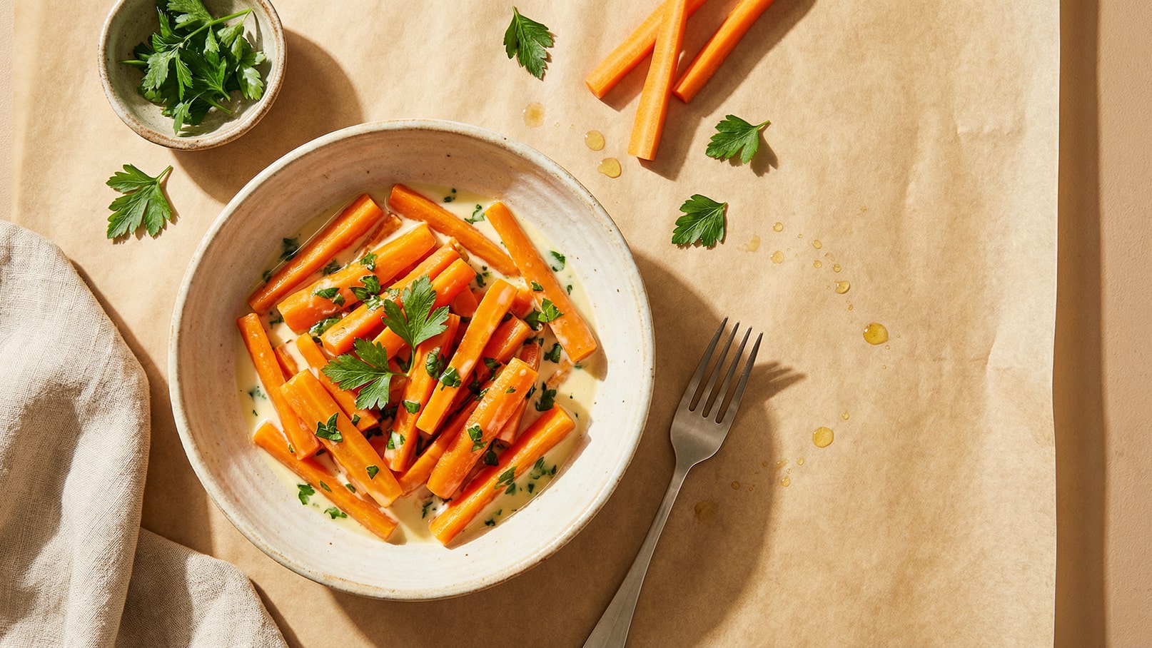 Eine Schüssel mit gekochten Karotten, garniert mit frischen Kräutern. Die Karotten sind in Stücke geschnitten und in einer cremigen Sauce angerichtet. Daneben liegt eine Gabel und ein kleiner Teller mit zusätzlichen Kräutern.