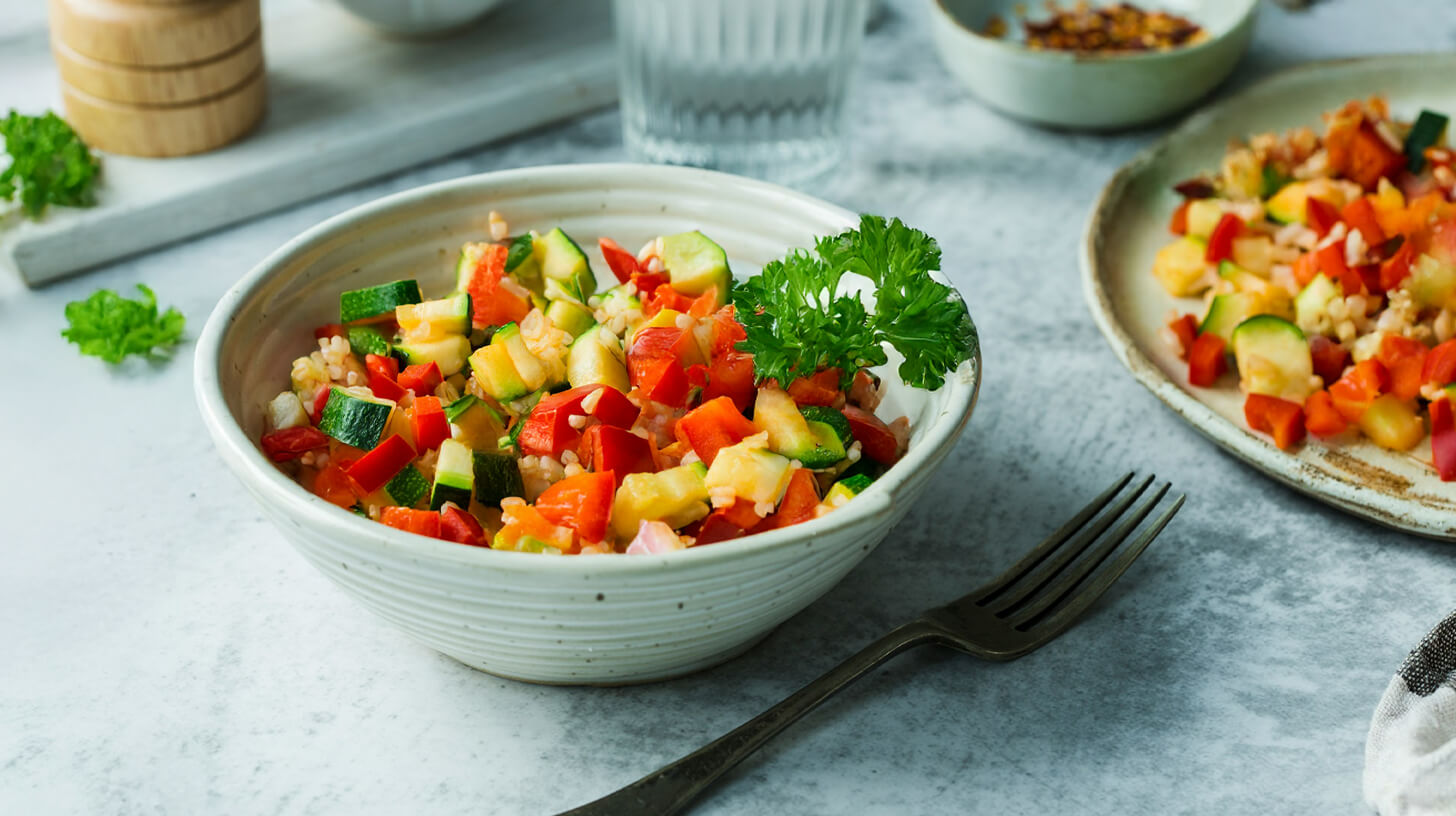 Eine Schüssel mit buntem Gemüsesalat, der Zucchini, rote Paprika, Gurken und Ananas enthält. Der Salat ist frisch zubereitet und mit einem Zweig Petersilie garniert.