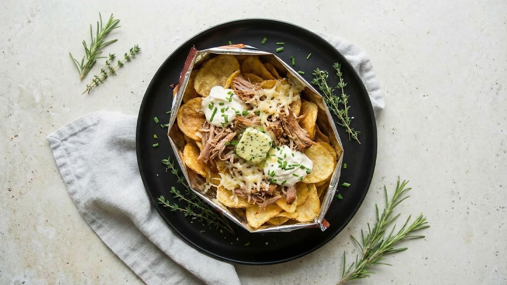 Eine Schüssel mit knusprigen Kartoffelchips, belegt mit zartem, zerrissenem Fleisch, geschmolzenem Käse, Sauerrahm und frischen Kräutern. Die Chips sind goldbraun und locker, während die cremigen Toppings und Kräuter für zusätzlichen Geschmack sorgen.
