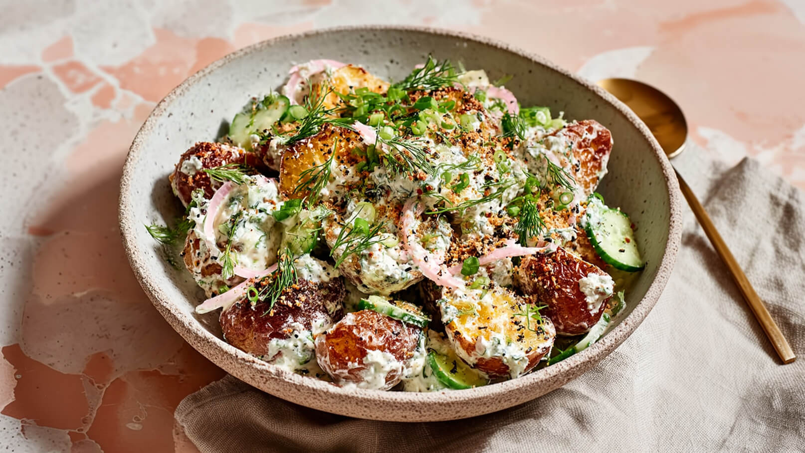 Eine Schüssel mit gebratenen Kartoffeln, garniert mit einem cremigen Dressing aus Joghurt, frischen Kräutern, gewürfeltem Gemüse und knusprigen Toppings. Die Kartoffeln sind goldbraun und crunchy, und die frischen Zutaten sorgen für einen farbenfrohen Kontrast.