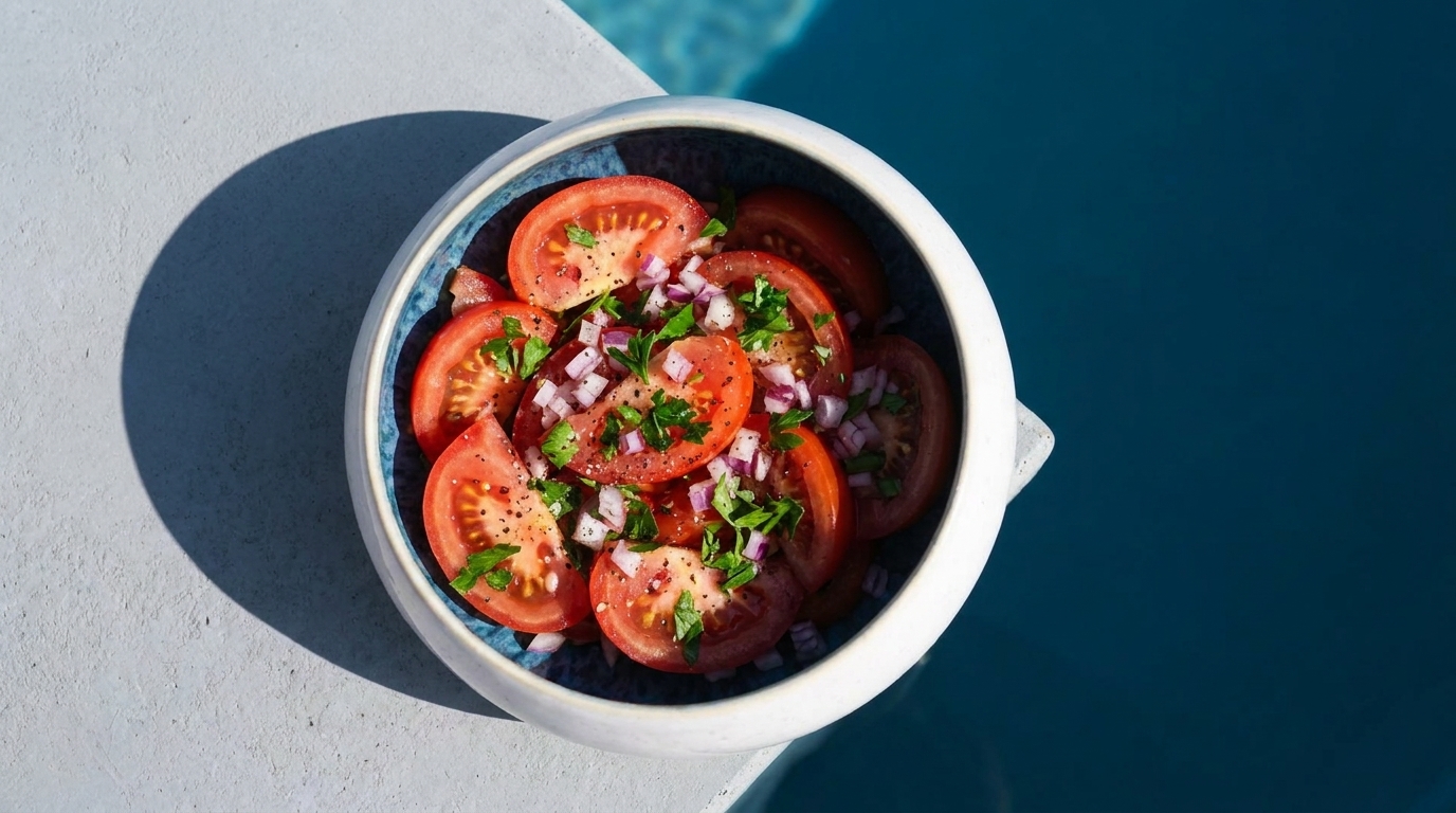 Tomatensalat in einer Schüssel: frische Tomatenscheiben mit gehackter roter Zwiebel, Petersilie und Gewürzen.