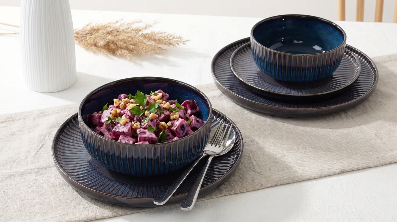 Dunkelblaue Keramikschalen auf Tellern, eine gefüllt mit lila Rote-Bete-Salat, Walnüssen und Petersilie; Besteck liegt daneben.