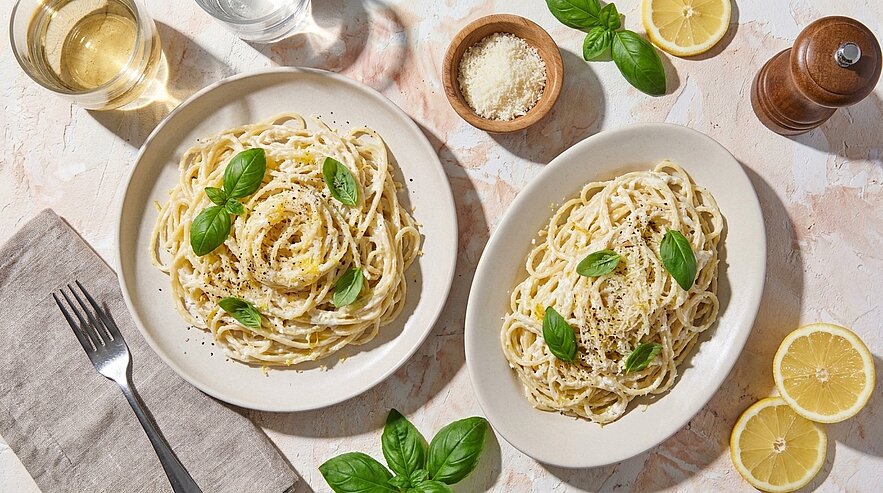 Zwei Teller Spaghetti in cremiger Zitronen-Parmesan-Sauce, bestreut mit schwarzem Pfeffer und garniert mit frischen Basilikumblättern.