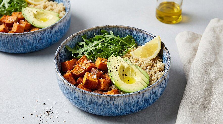 Eine Schüssel mit Quinoa, gewürfeltem Süßkartoffel, frischem Rucola, Avocado und Zitronenscheiben. Die Zutaten sind appetitlich angerichtet und vermitteln ein gesundes, ausgewogenes Mahl.