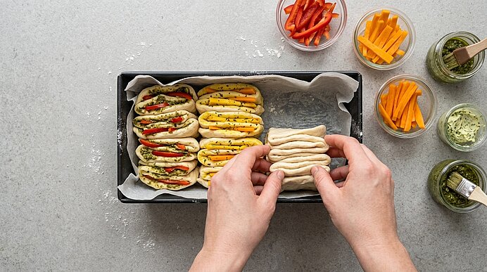 Zwei Hände legen gefalteten, mit Pesto und Gemüse belegten Teig in eine Kastenform.