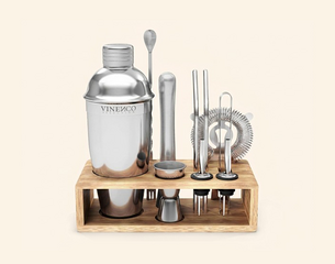 Edelstahl-Cocktail-Set auf Holzständer: Shaker, Stößel, Barsieb, Bar-Löffel, Jigger (Doppelmaß) und zwei Flaschen-Ausgießer.