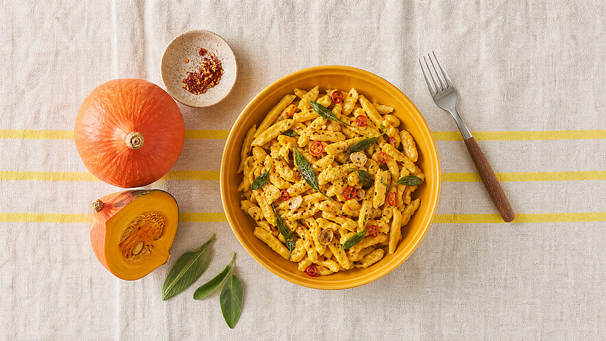 Schüssel mit cremiger Kürbis-Penne, gewürzt und garniert mit frischen Salbeiblättern und roten Chiliringeln.