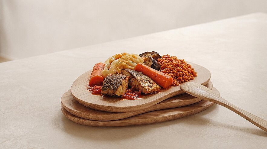 Holzservierbrett mit einer Portion warmer Speisen: gebratene Filetstücke, ganze Karotten, Kartoffelpüree und Bulgur in Tomatensauce.