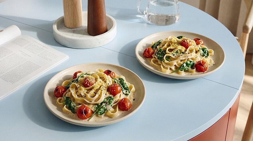 Zwei Teller Tagliatelle mit Spinat, gebratenen Kirschtomaten, geriebenem Parmesan und schwarzem Pfeffer, serviert auf einem Tisch.