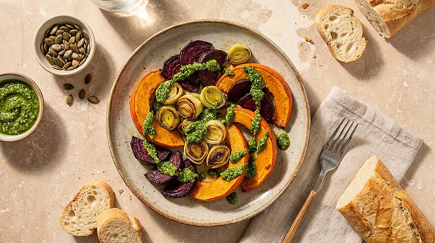 Teller mit gebratenen Kürbisscheiben, Rote-Bete-Scheiben und zusammengerollten Lauchstücken, garniert mit grüner Kräuterpesto.