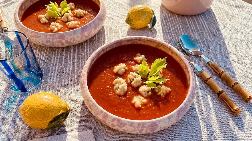 Zwei Schalen cremige Tomatensuppe, jeweils mit kleinen Klößchen und Sellerieblättern garniert.