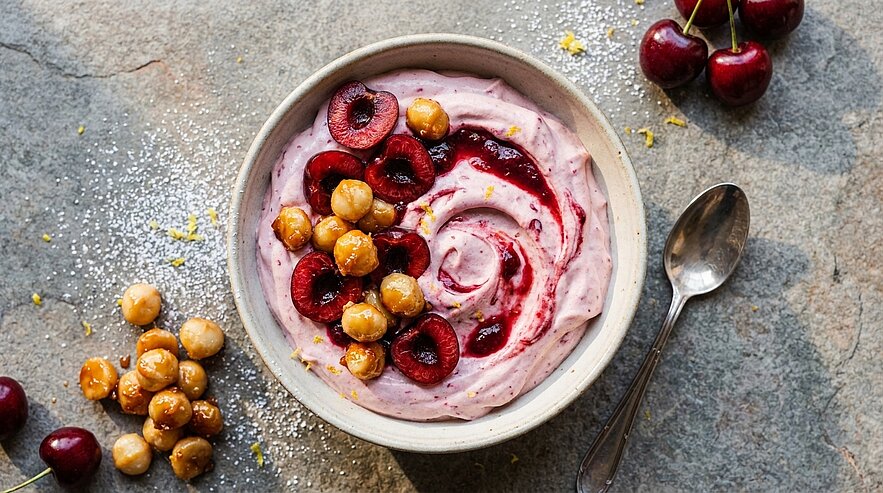 Schale mit rosa Joghurt-Bowl, garniert mit halbierten Kirschen, Kirschsoße und knusprigen, gerösteten Nüssen.