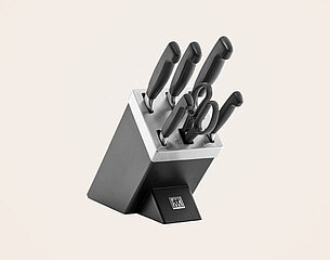Ein Messerset in einem schwarzen Messerblock. Der Block enthält mehrere Messer mit schwarzen Griffen sowie eine Küchenschere, alles ordentlich angeordnet. Der Untergrund ist hell und unifarben.