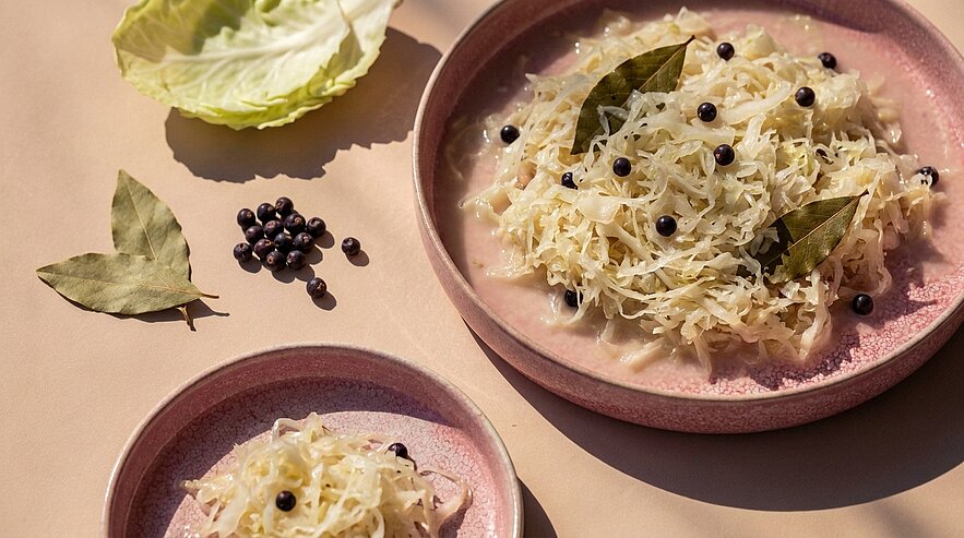 Zwei Schalen mit Sauerkraut, garniert mit Lorbeerblättern und Wacholderbeeren.
